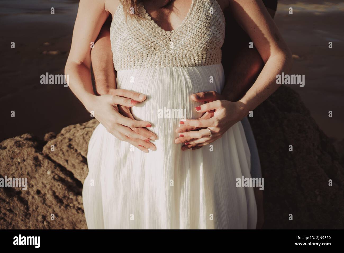 A man holding his beautiful pregnant partner's belly on a beach in