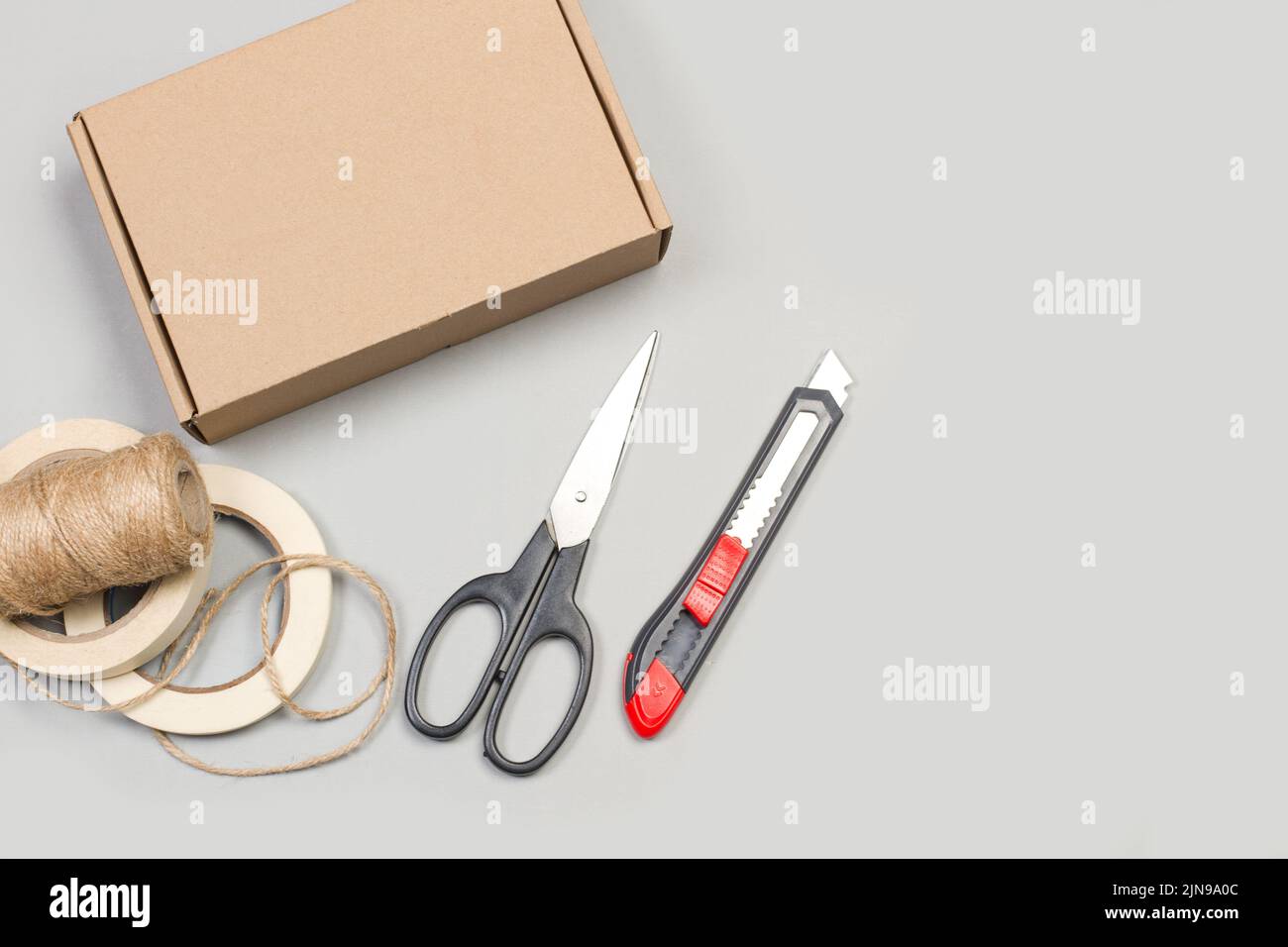 Scissors, cutter, masking tape and a cardboard box on a gray background