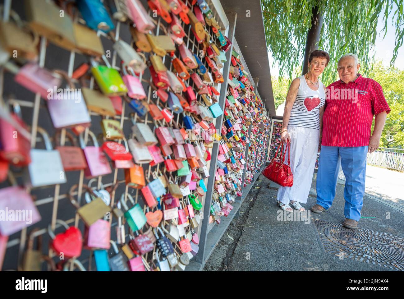 Heilbronn, Germany. 10th Aug, 2022. On the 'Day of the Love Lock' in Heilbronn, Ingrid and Hans Hey stand next to numerous love locks on the Götzenturm Bridge. More than a decade ago, 87-year-old initiator Hans Hey and his wife were the first to put up a love lock on the railing of the Götzenturm bridge to mark their golden wedding anniversary - today, around 15,000 locks hang there. Credit: Christoph Schmidt/dpa/Alamy Live News Stock Photo