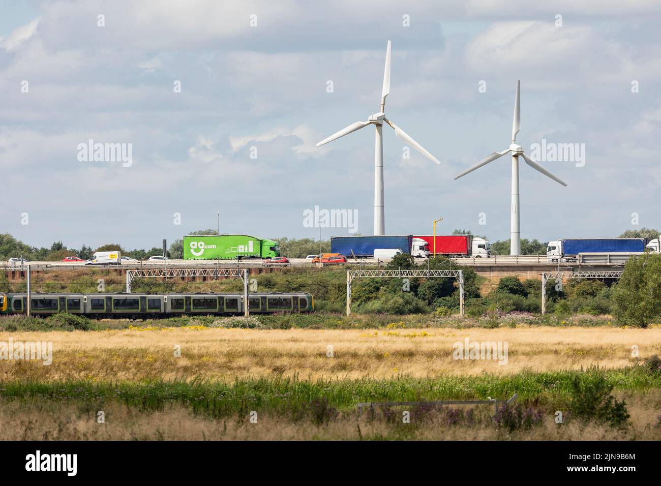 Stafford-Staffordshire-United Kingdom April 27, 2022  green marshland neighbours a busy motorway and train line, with two wind turbines, Stock Photo