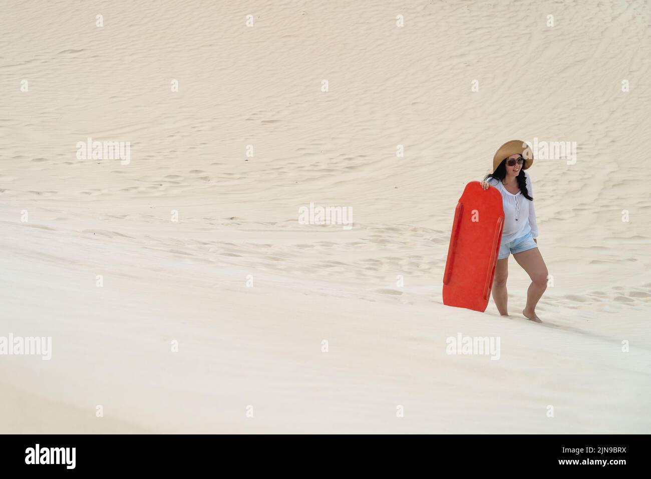 Woman climbing up a sand dune with a sandboard, Kangaroo Island, South Australia Stock Photo