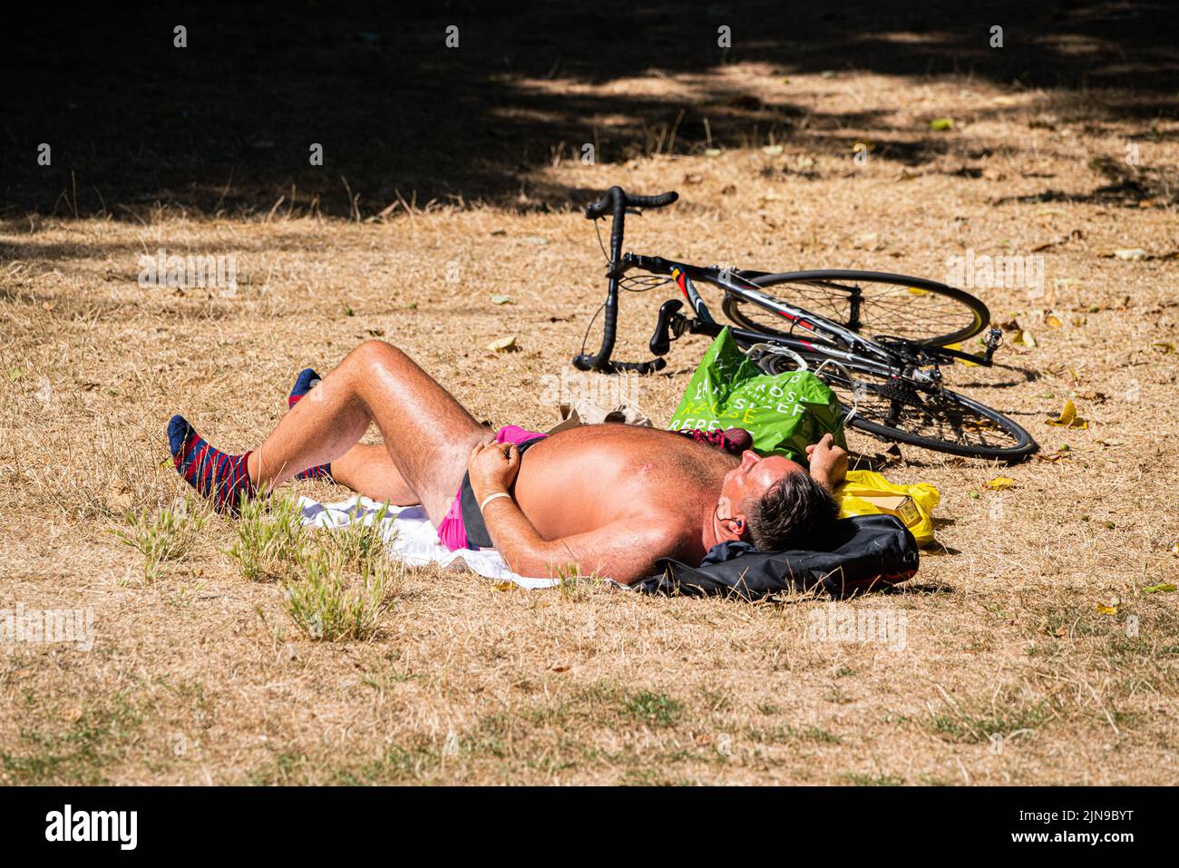 Putney London, UK. 10th Aug, 2022. A man sunbathing next to his bicycle on the parched grass in Bishop's park, Putney, south west London. The Met Office has issued an amber extreme heat warning for southern and central England and parts of Wales from Thursday until Sunday as temperatures are expected to reach up to 35C in some parts of the country Credit. Credit: amer ghazzal/Alamy Live News Stock Photo
