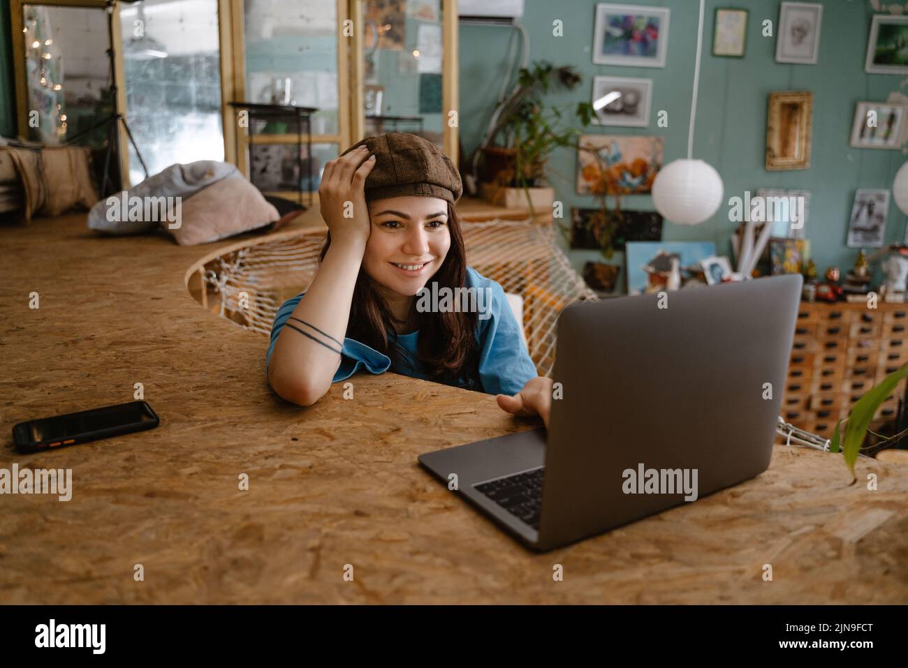 Young woman artist using laptop while resting in hammock at her studio indoors Stock Photo