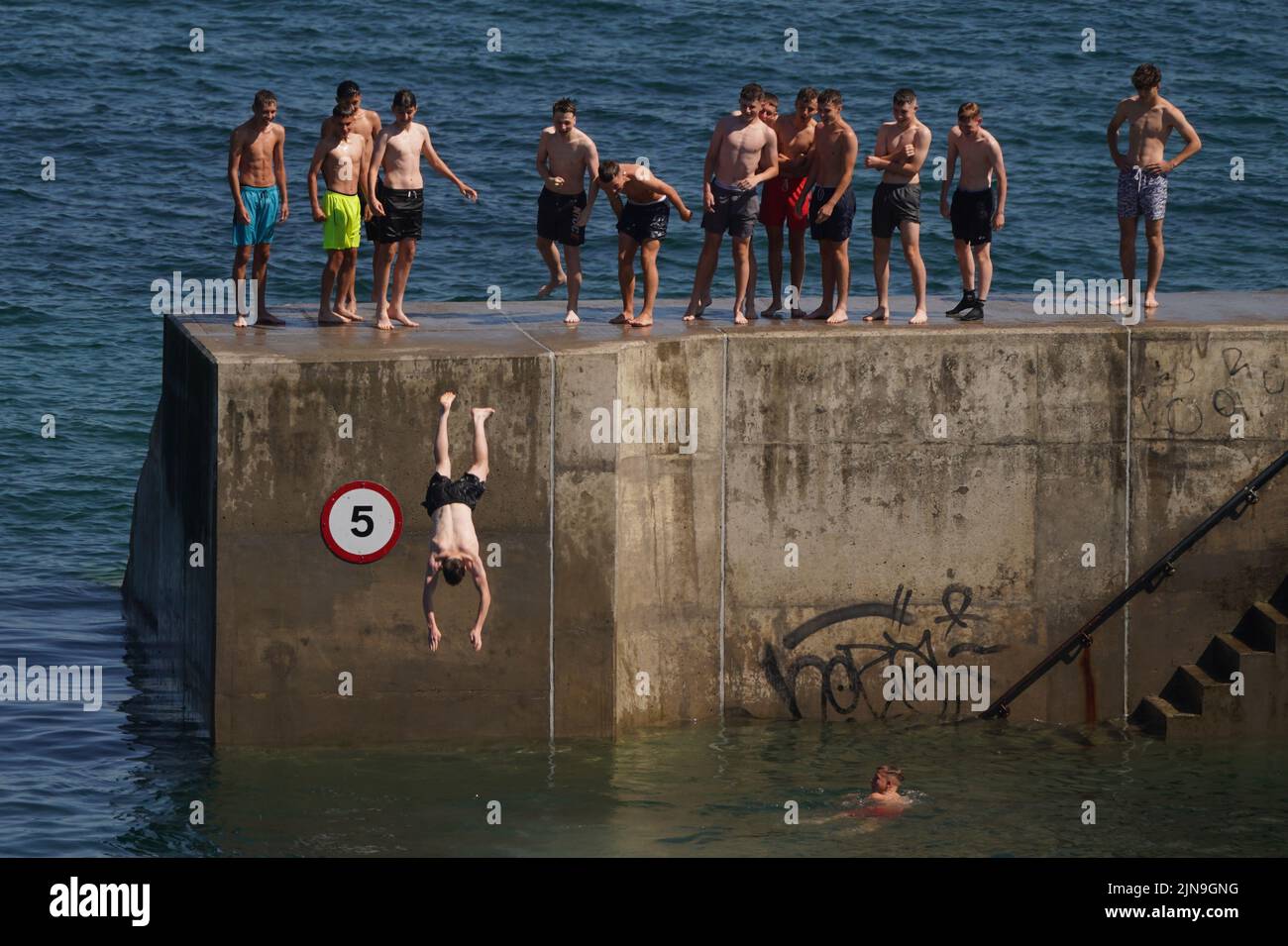 A group of young men cool off in the hot weather by diving into the water at Cullercoats Bay in North Tyneside. The Met Office has issued an amber warning for extreme heat covering four days from Thursday to Sunday for parts of England and Wales as a new heatwave looms. Picture date: Wednesday August 10, 2022. Stock Photo