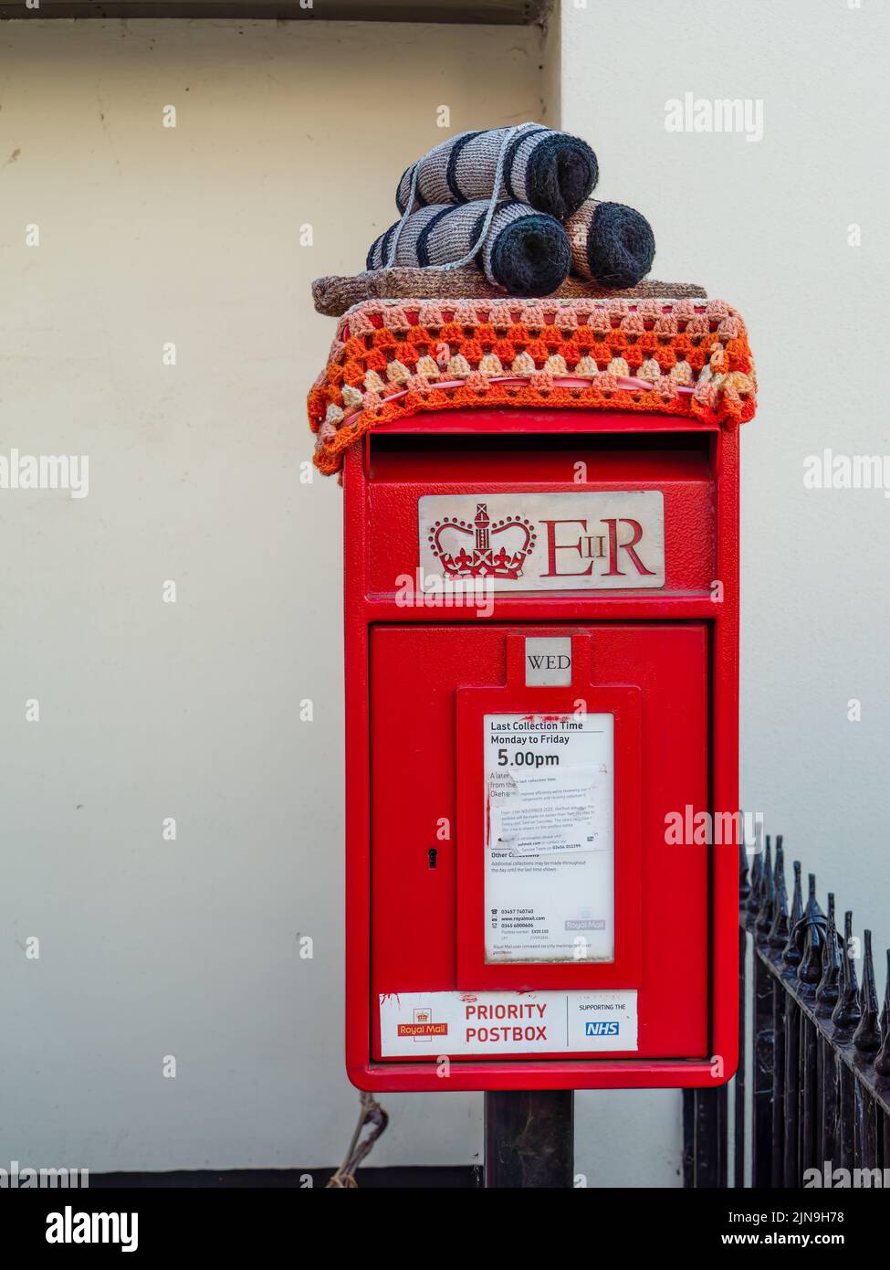 HATHERLEIGH, DEVON, ENGLAND - AUGUST 9 2022: Red post box. It is adorned with crochet tar barrels on sled, part of the town's annual festival. Stock Photo