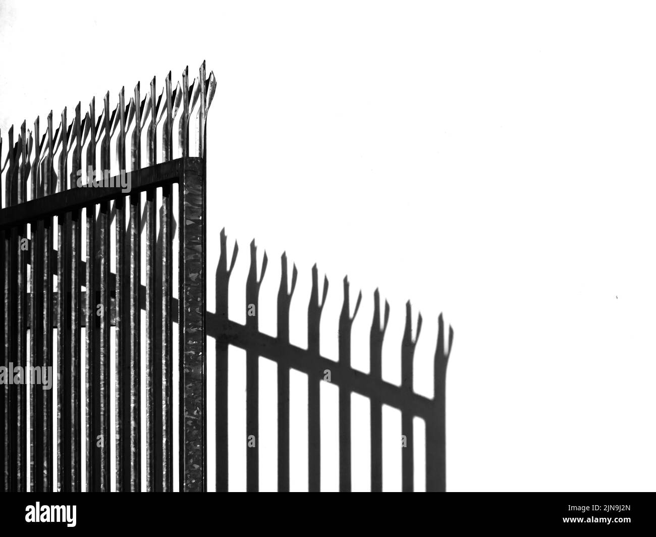 Spiked and barbed metal gate in fence with shadow. Security concept, background. Stock Photo