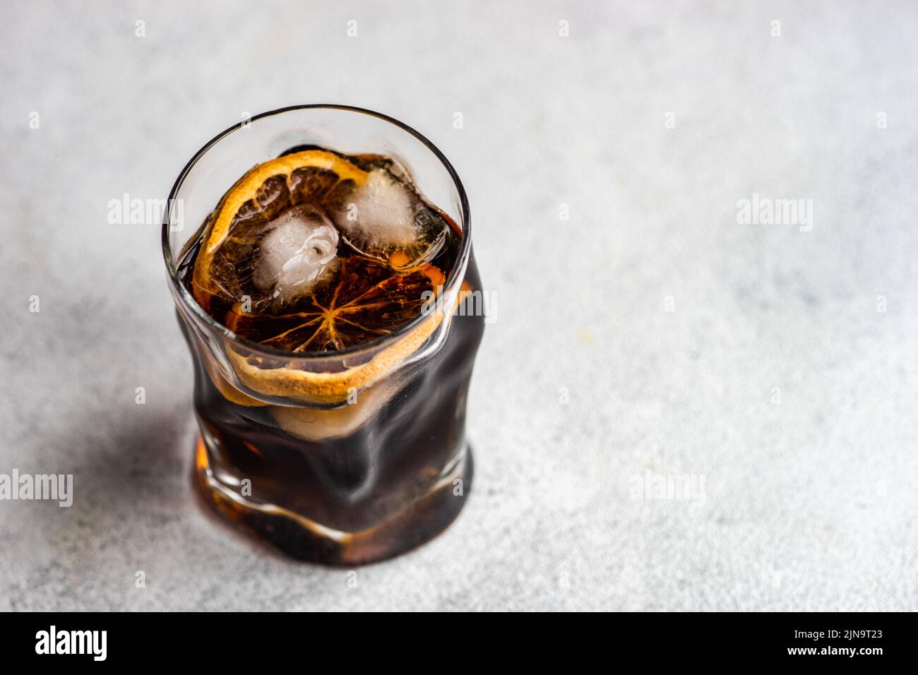 Alcohol cocktail with coke in the glass with orange and ice on grey