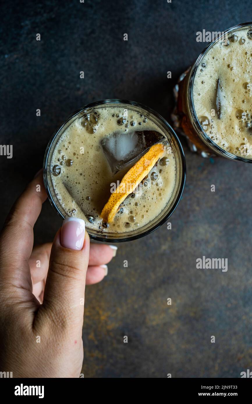 Alcohol cocktail with coke in the glass with orange and ice in woman