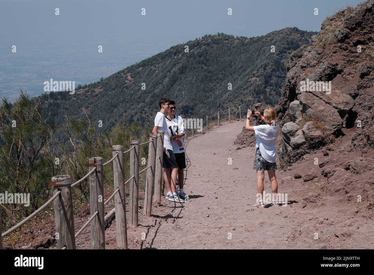 A mum and two sons pose for a family phone picture on the walkway at the top of Mount Vesuvius Italy looking out to the view towards Naples. Stock Photo
