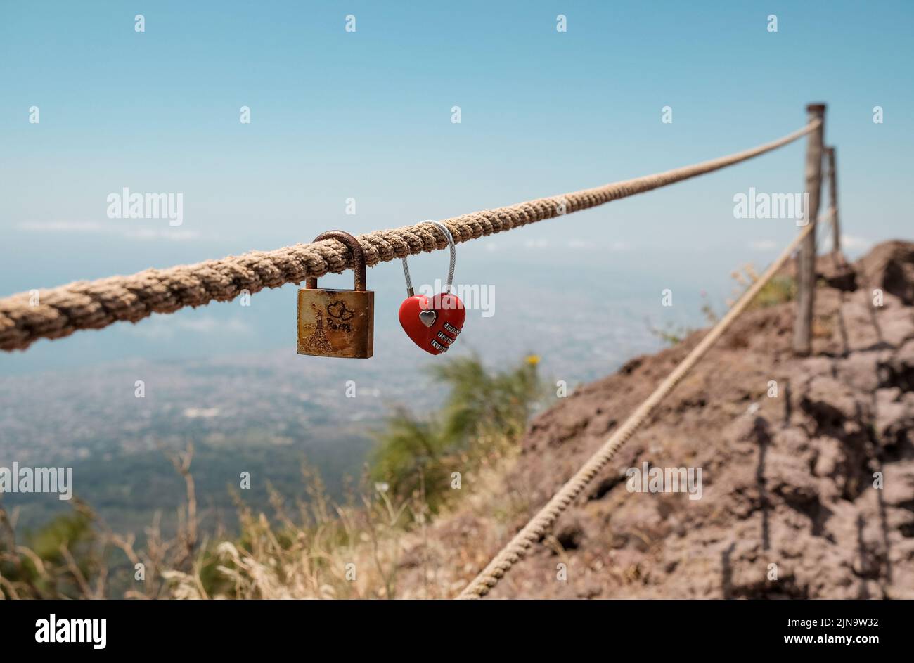 Love locked padlocks on the rope protecting you from the drop at Mount Vesuvius Volcano in Italy. The padlock at the front has Paris Eiffel Tower on. Stock Photo