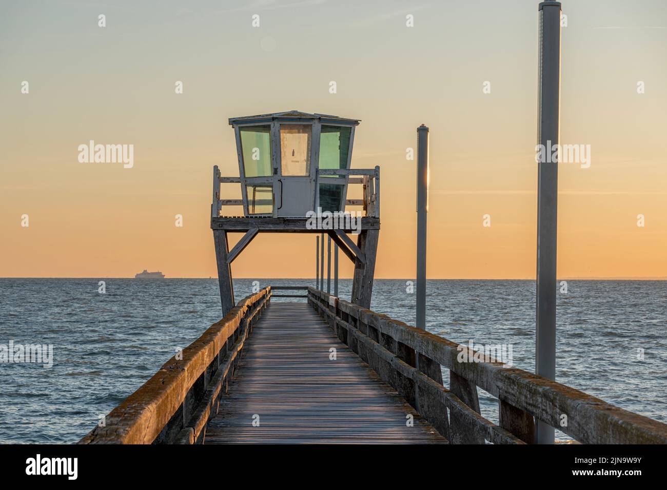 View of a wooden pier in front of the sea, a colorful sunrise and Le Havre city buildings far away Stock Photo