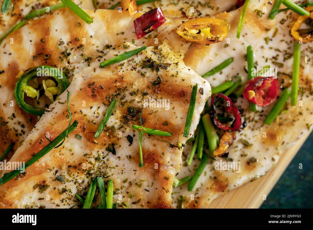 Macro close-up of grilled chicken breast cooked with three different colors chili peppers and aromatic herbs. Stock Photo