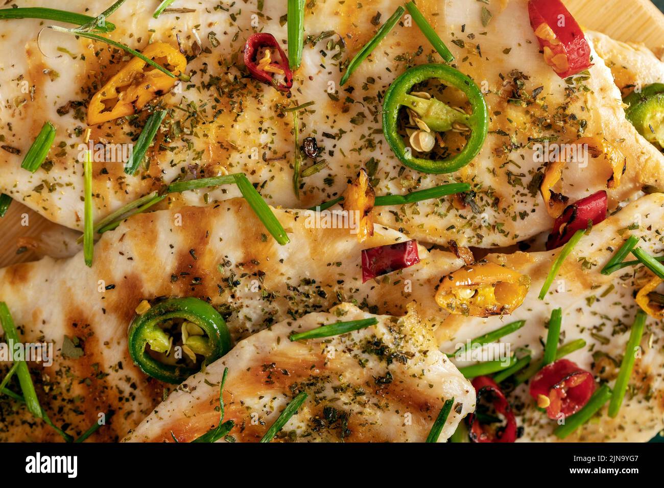 Macro close-up of grilled chicken breast cooked with three different colors chili peppers and aromatic herbs. Stock Photo