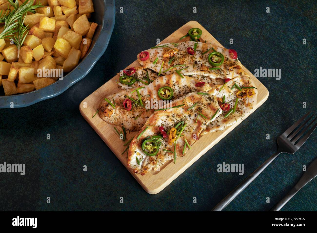 Grilled chicken breast cooked with three different colors chili peppers and aromatic herbs. Baked potatoes on the background. Stock Photo