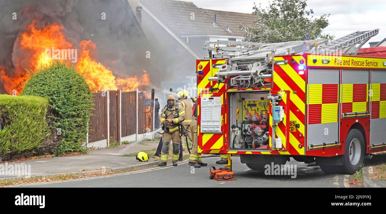 Fire engine tender Essex Fire and Rescue Service fire brigade firemen firefighters at burning house fire flames ablaze black smoke close up England UK Stock Photo