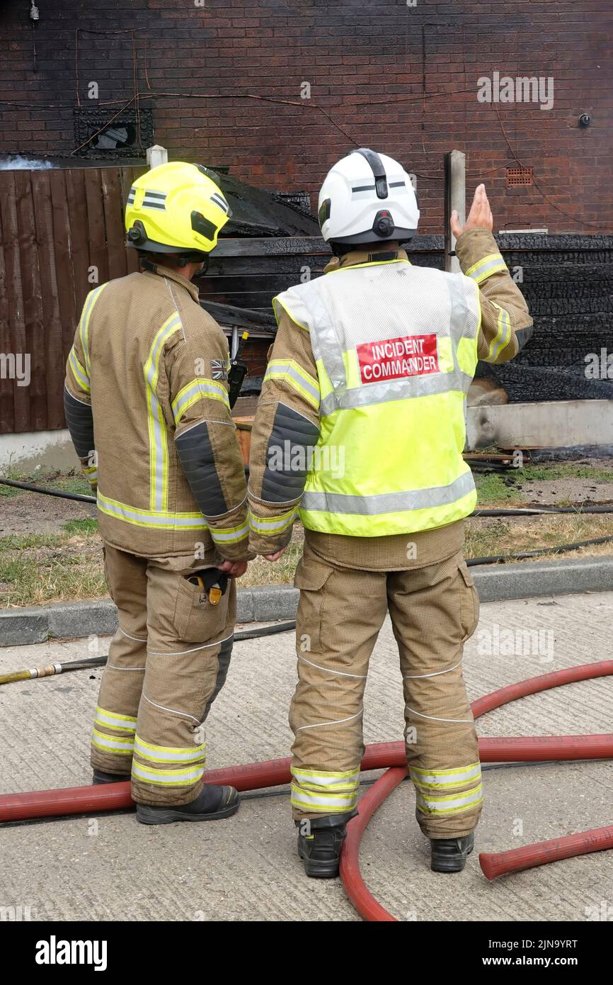Back view Essex Fire and Rescue Service fire brigade fireman firefighter house building fire with incident commander blaze under control aftermath UK Stock Photo