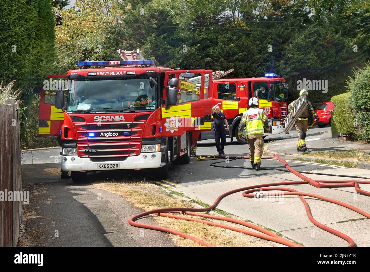 Essex fire and rescue service fire brigade firemen attending house fire with two fire engines & firefighters in residential street England UK Stock Photo