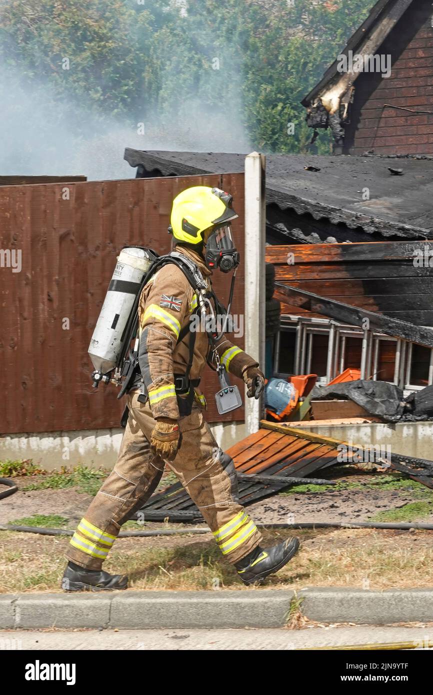 Firefighter firemen protective clothing & helmet wearing breathing apparatus equipment about to search interior smouldering building fire England UK Stock Photo