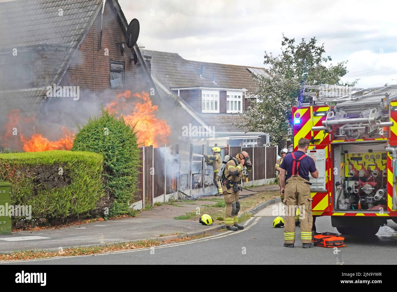 Essex Fire and Rescue services fire brigade firemen at house fire  firefighters in protective clothing start work on flames beside fire engine  UK Stock Photo