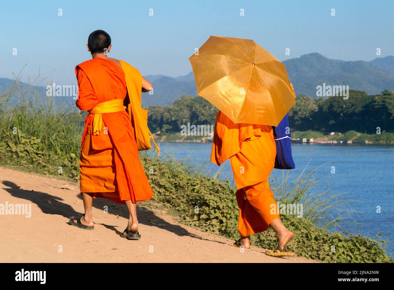 Monks with umbrella on the banks of the Mekong river, Luang Prabang, Laos Stock Photo