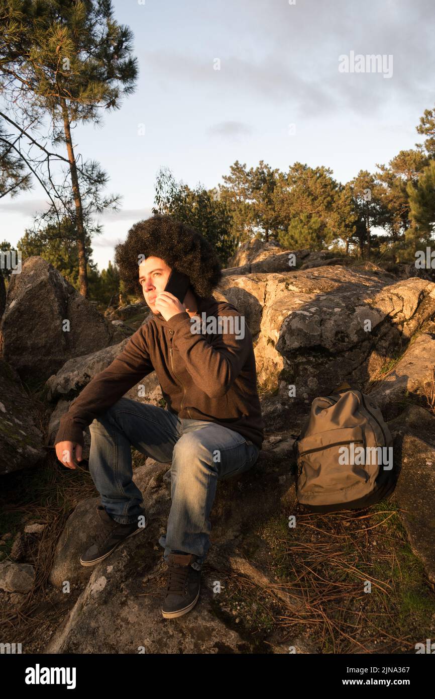 Young man with afro hair talking on smartphone sitting on a rock Stock Photo