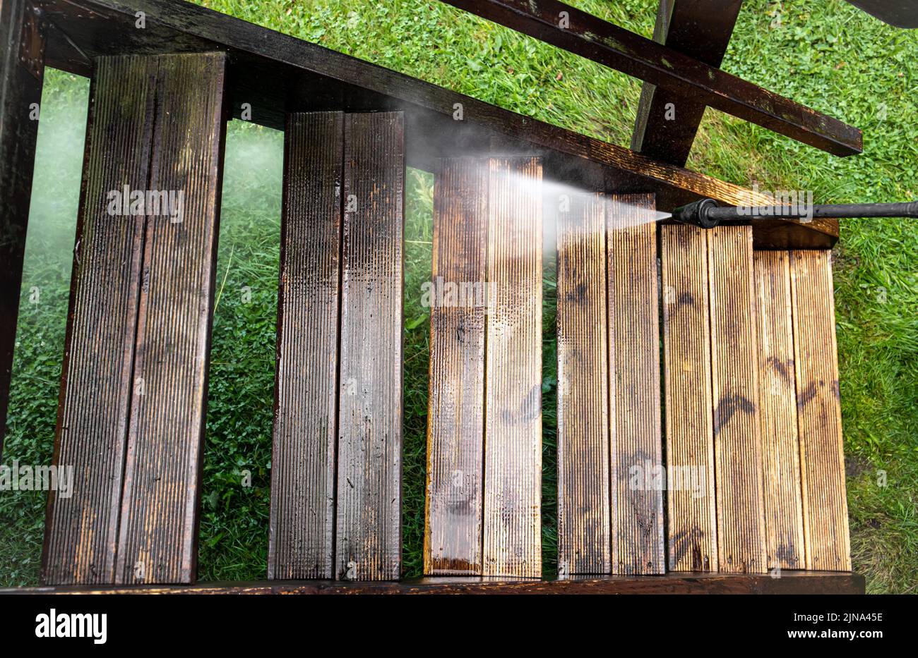Close up view of using pressure washer to clean impregnated wood terrace stairs outdoors in the spring. Before cleaning and after, big contrast. Stock Photo