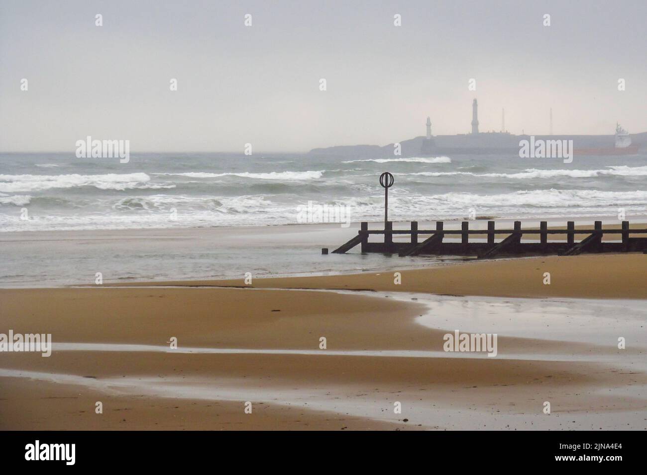 View over the Deserted sandy Aberdeen Beach, with the lighthouse in the mist in the background Stock Photo
