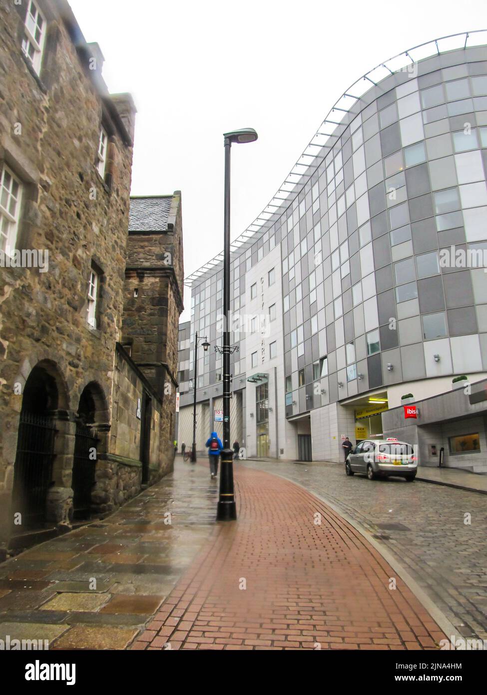Contrasts in Aberdeen, looking up a city street with an old stone building on the one side and a modern glass office building on the other side. Stock Photo