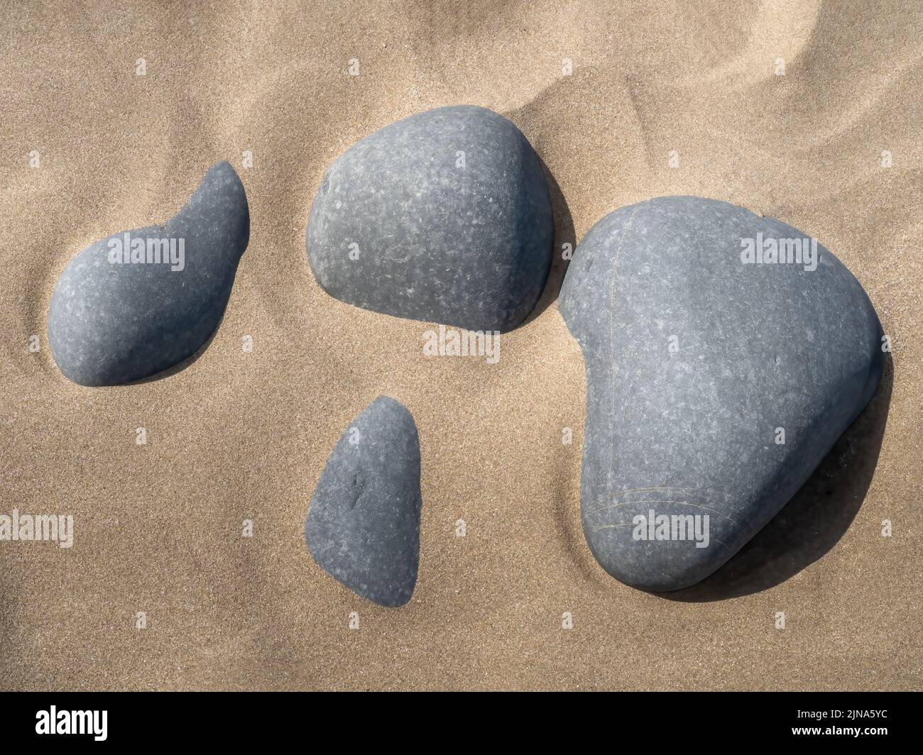 Grey pebbles on golden sandy beach, abstract effect image. Stock Photo