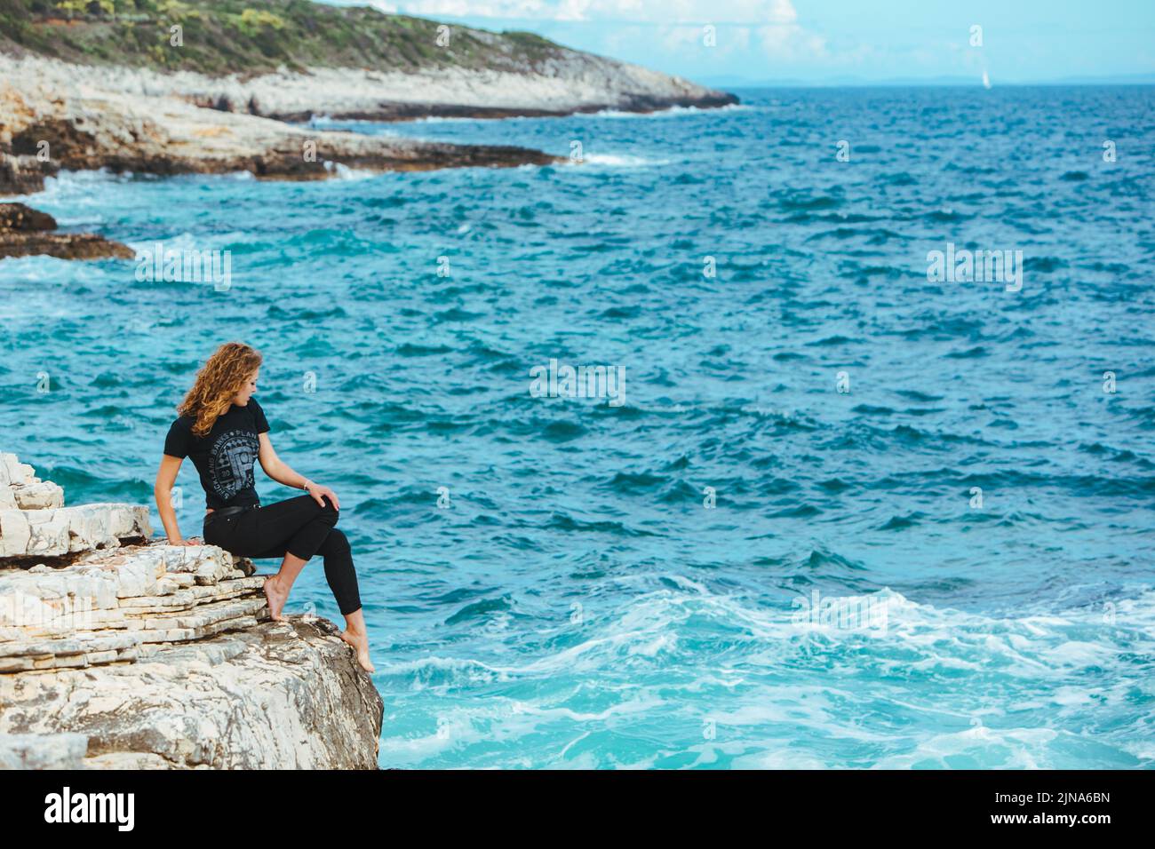 young slim woman sitting on the cliff edge looking at sea Stock Photo ...