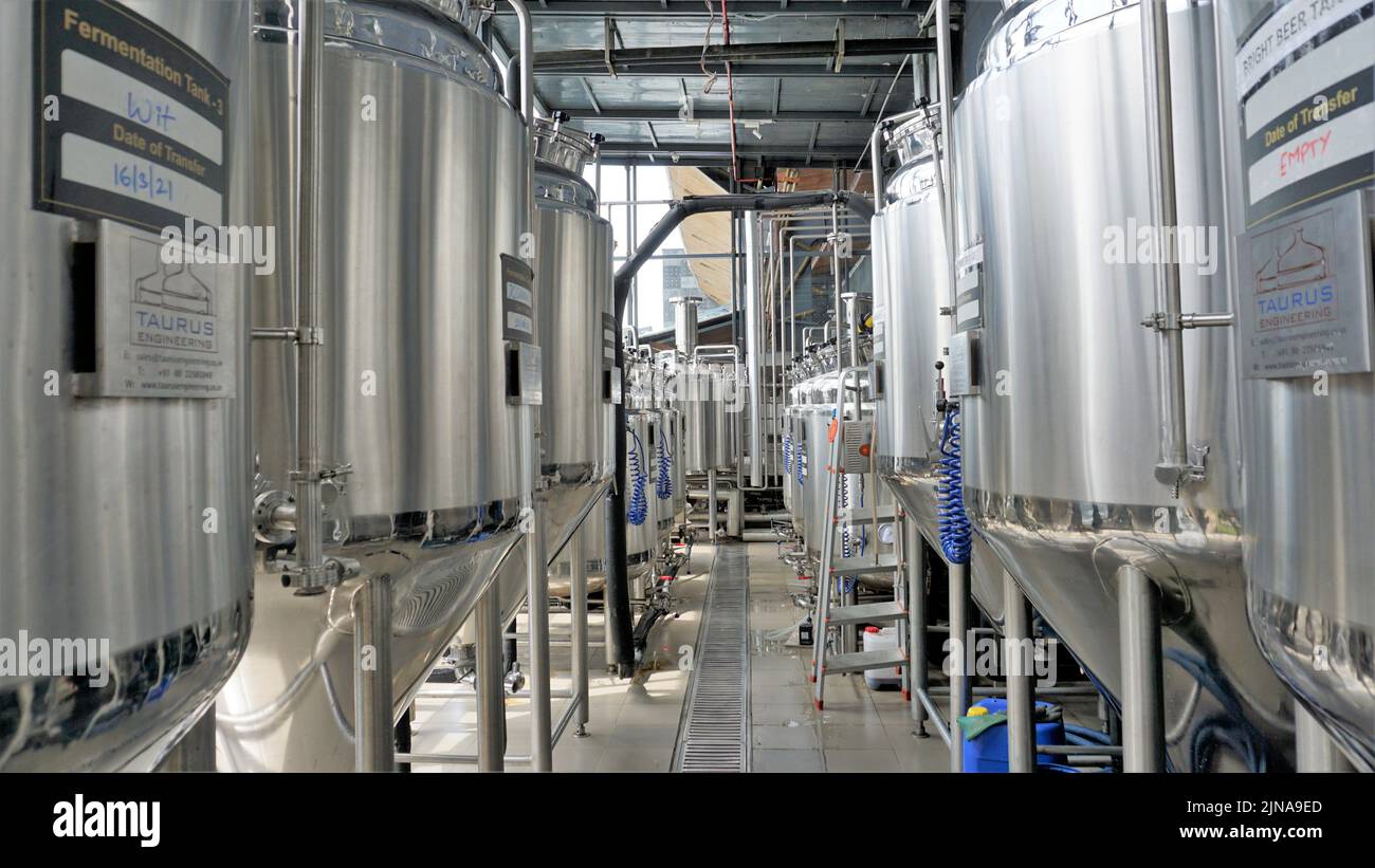 Row of shiny metal micro brewery tanks or Fermentation mash vats in Brewery factory. Modern beer plant with brewering kettles, tubes and tanks made of Stock Photo
