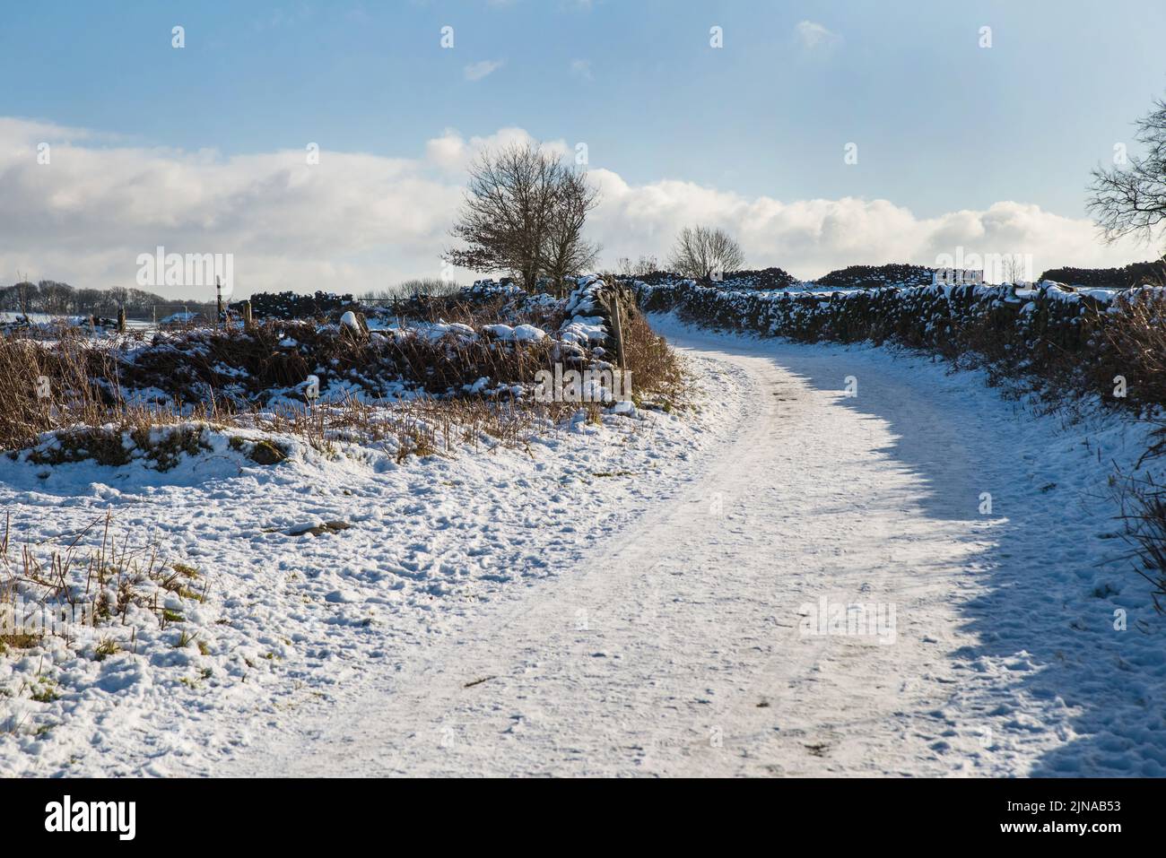 A country lane with drystone walls either side after a fall of snow, Derbyshire, England Stock Photo