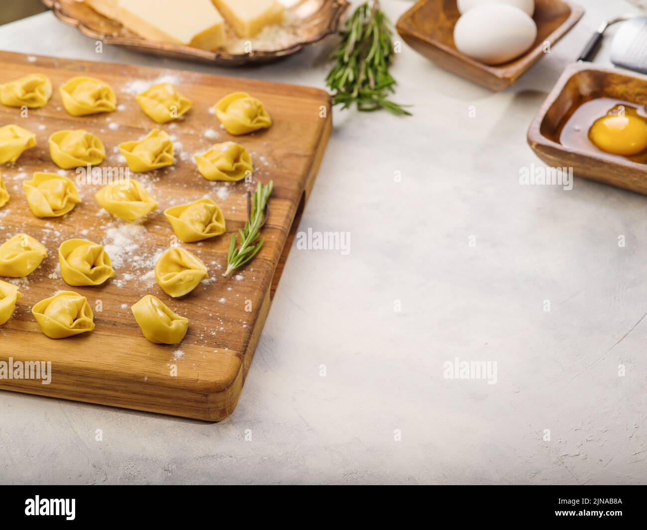 Cooking homemade ravioli, dumplings stuffed with minced meat - pork and beef. Dumplings on a wooden cutting board, ingredients, sprigs of rosemary on Stock Photo