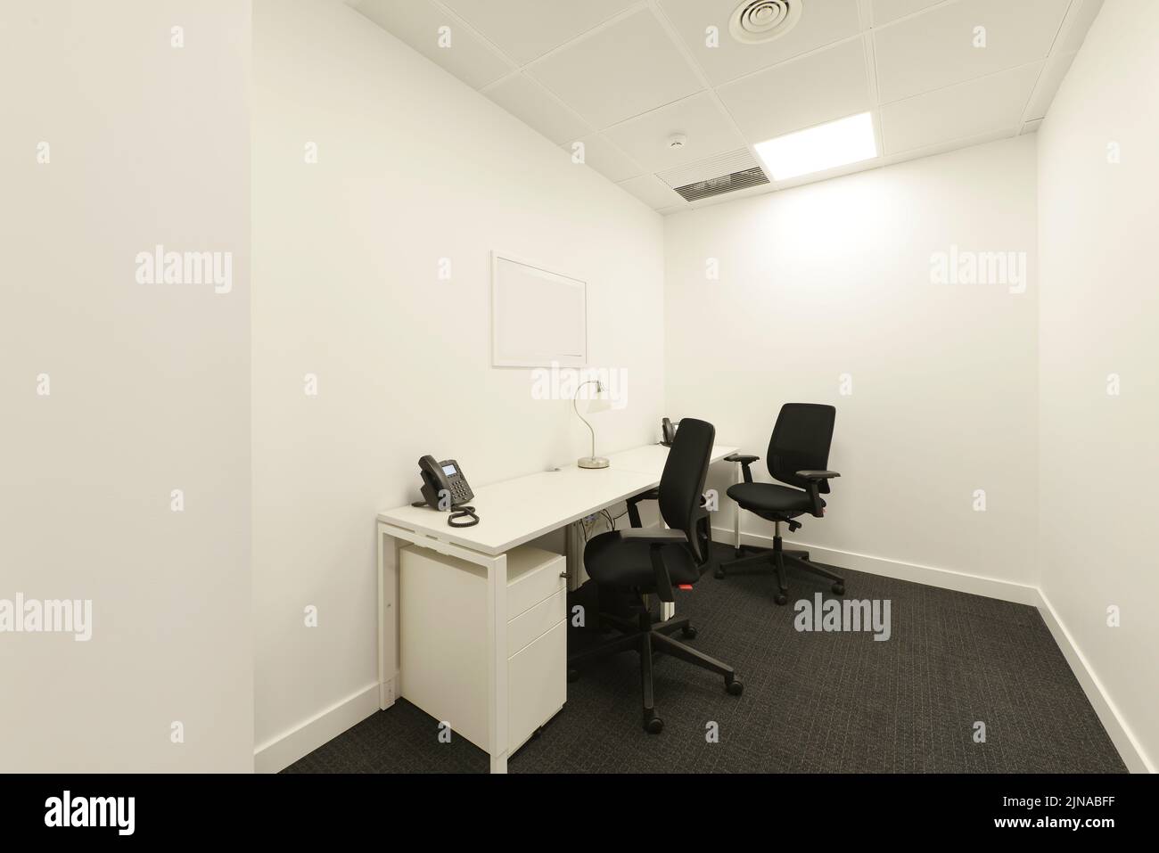 Small office cubicle with white desk and twin black chairs Stock Photo