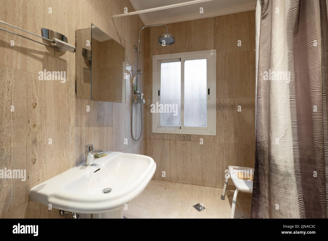 Bathroom with white porcelain sink, marble tiles and shower with seat Stock Photo