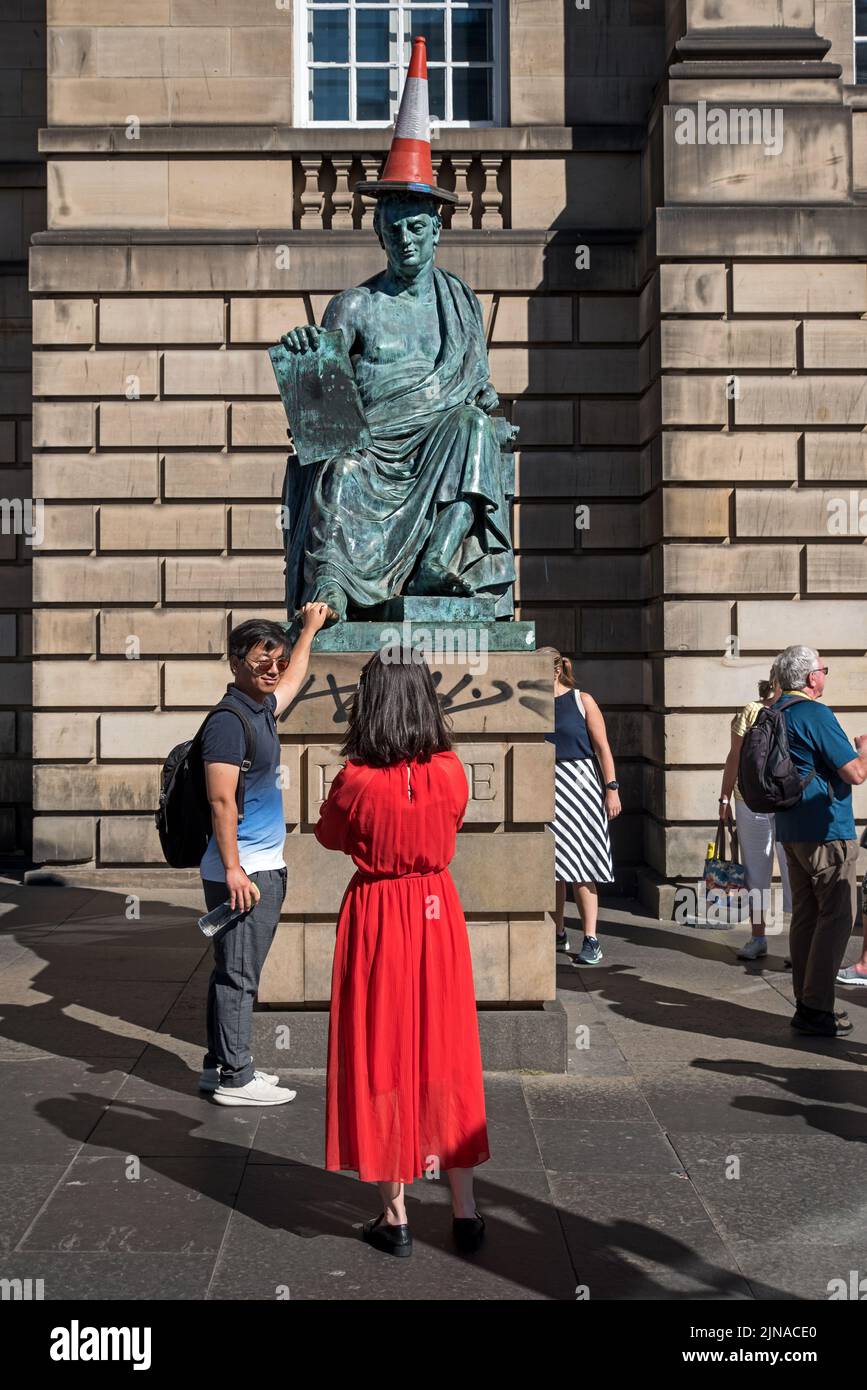A tourist rubs the toe on the statue of the Scottish Philosopher David Hume, with traffic cone, on Edinburgh's Royal Mile. Stock Photo