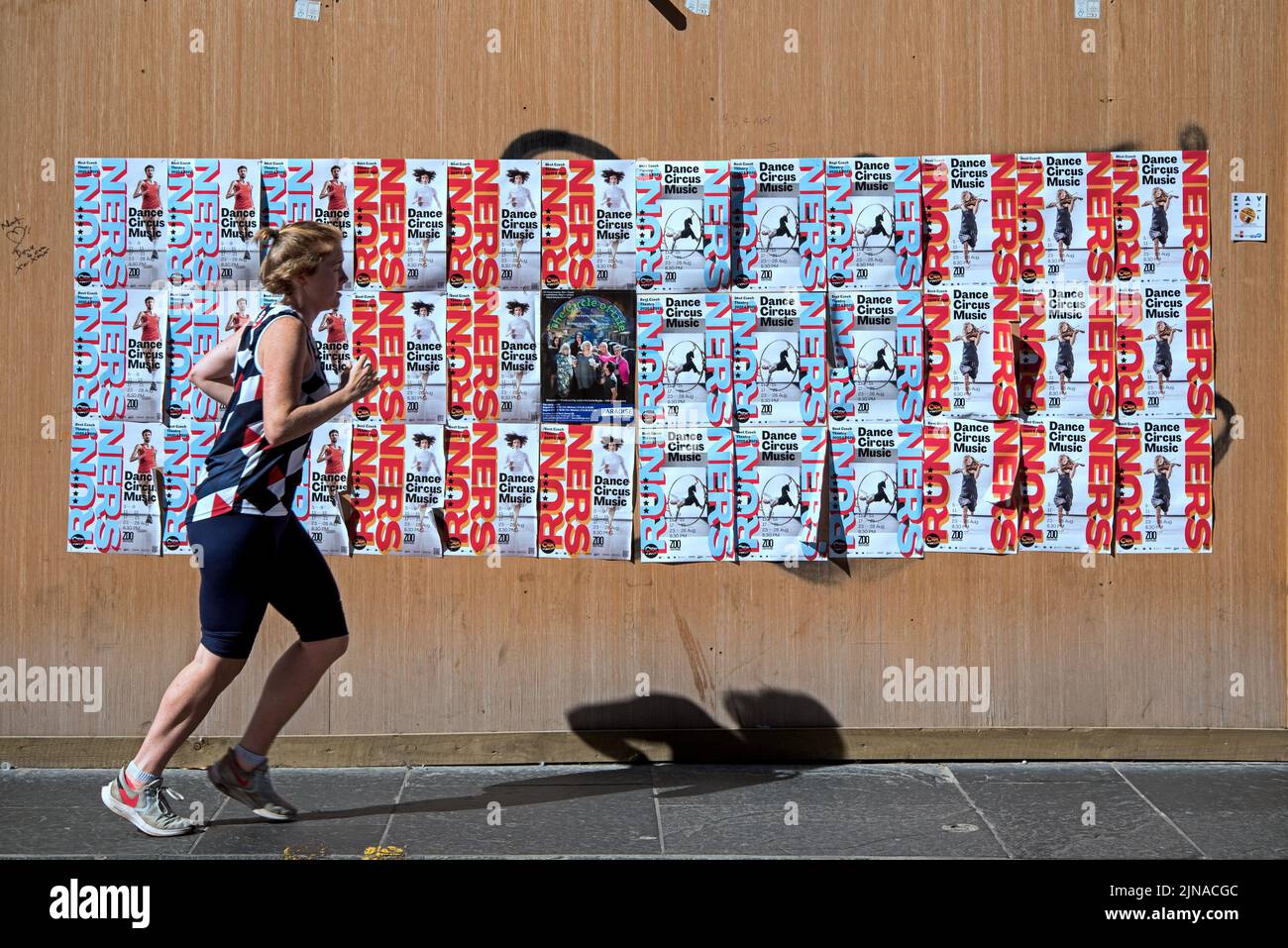 A runner runs by posters for Runners featuring Dance, Physical Theatre and Circus by the Czech Company Cirk La Putyka at the Edinburgh Fringe 2022. Stock Photo