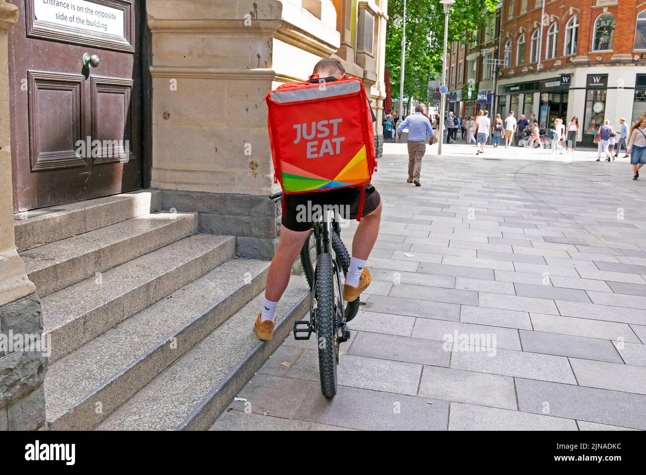 Just Eat fast food sign logo on back of rucksack on cyclist man courier delivery bike  in Cardiff City street Wales UK   KATHY DEWITT Stock Photo