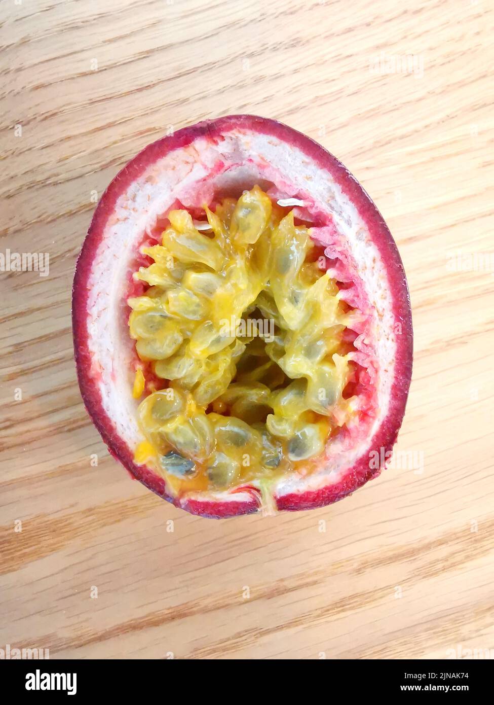 Half passion fruit showing yellow seeds and pink skin lying on wooden table Stock Photo
