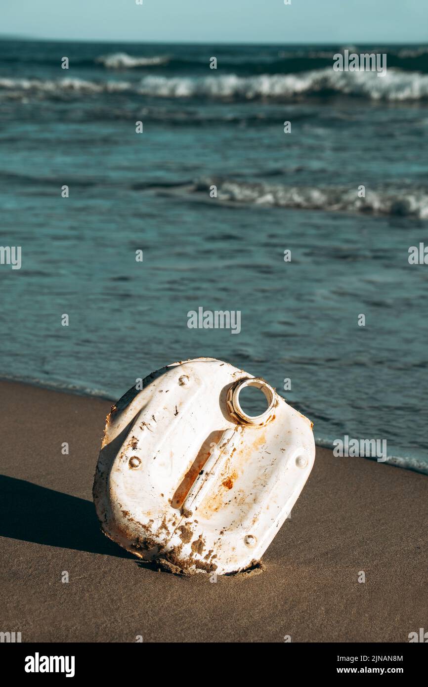 a piece of a used white plastic bottle on the wet sand of a beach, brought back to the seashore by the ocean Stock Photo