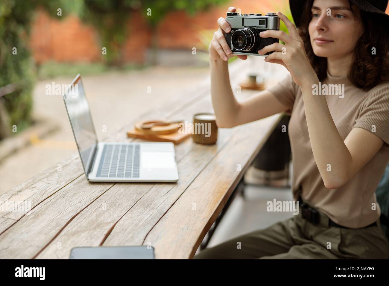 Smiling female traveler using photo camera while sitting in cafe outdoors Stock Photo
