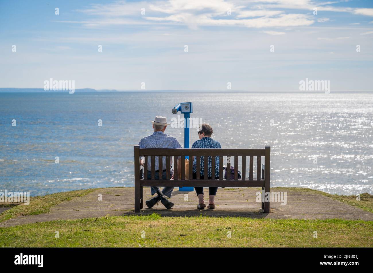 Elderly couple staring out at the ocean sitting on the bench on the ...