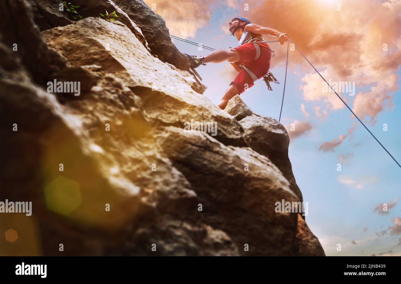 Muscular climber man in protective helmet abseiling from cliff rock