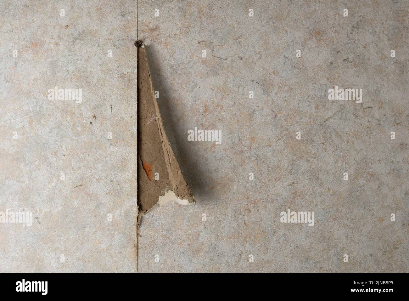Aged room wall with torn wallpaper. Old plaster is visible from under the wallpaper. Grunge vintage background. Old house interior Stock Photo