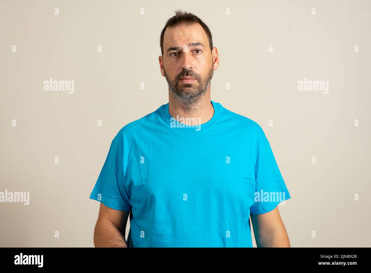 Isolated photo of handsome man with fashionable beard, mustache and hairstyle, wears casual blue t-shirt, poses in studio on beige background. Stock Photo