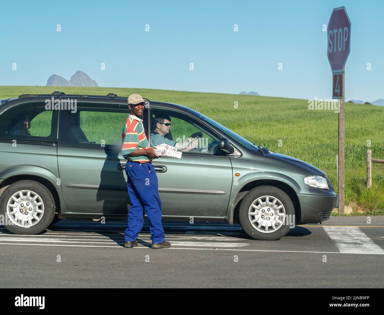 Cape Town South Africa August 26 2007: Man turns and smiles standing by stopped car trying to sell strawberries and earn a living. Stock Photo