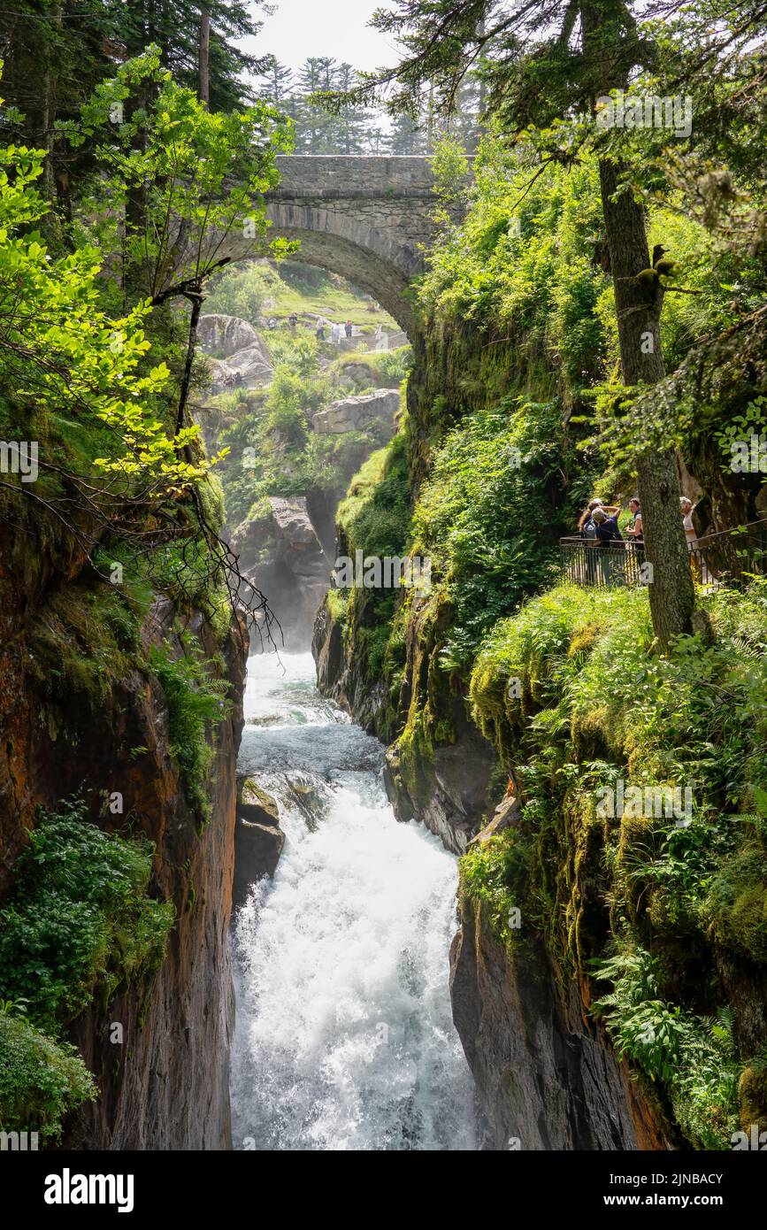a waterfall and river pour through steep-sided rock gorge with white water crashing over boulders and stone bridge overhead, Pont e'Espagne Pyrennes Stock Photo