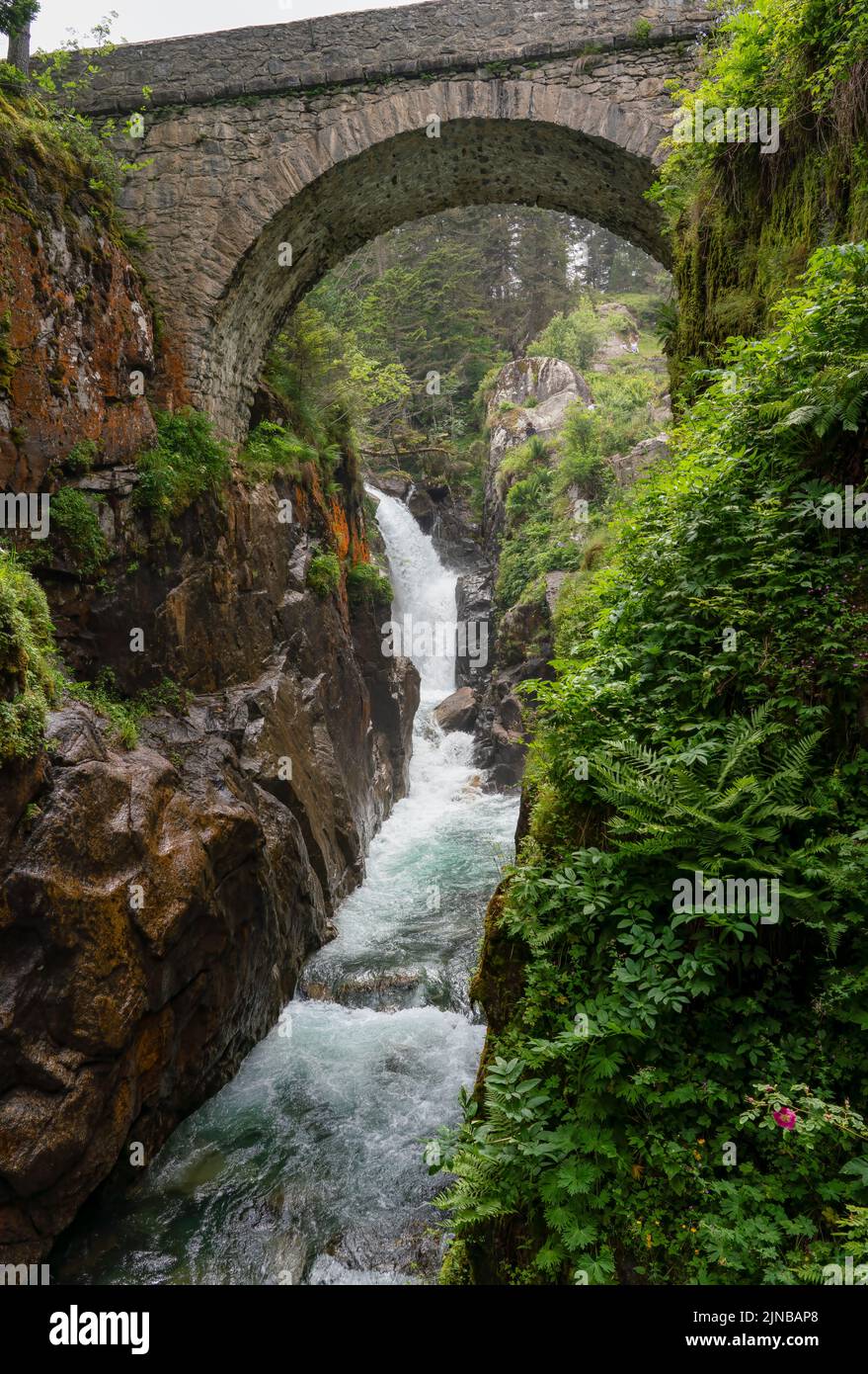 a waterfall and river pour through steep-sided rock gorge with white water crashing over boulders and stone bridge overhead, Pont e'Espagne Pyrennes Stock Photo