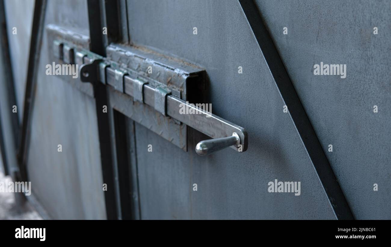 Old gray metal gate with a deadbolt. Shiny polished bolt handle close-up. Traces of corrosion on metal. Aging process. rusty surface. Home security. Outdoors. Stock Photo