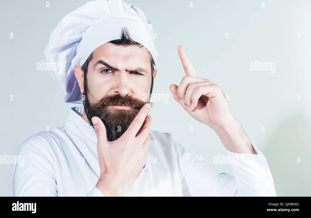 Professional chef pointing finger up. Pensive bearded man in cook uniform. Cooking food new idea. Stock Photo